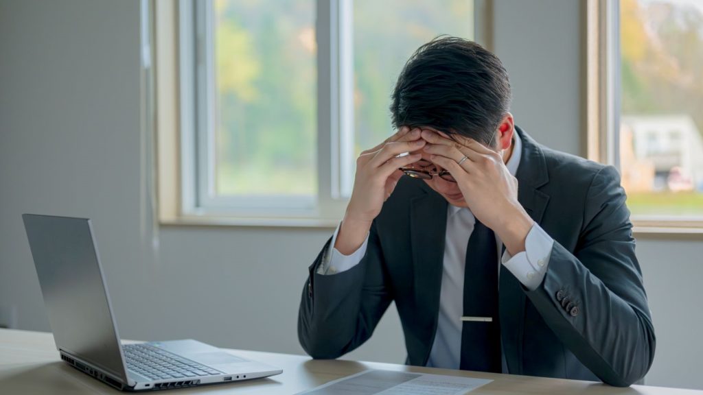 PC前で額を抑えるスーツ姿の男性