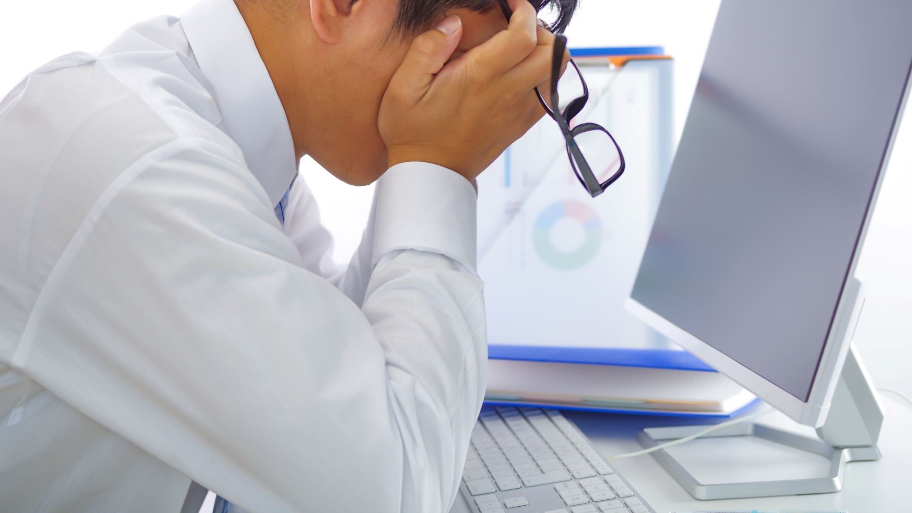 眼鏡を持った、PCの前で顔を手で覆う男性