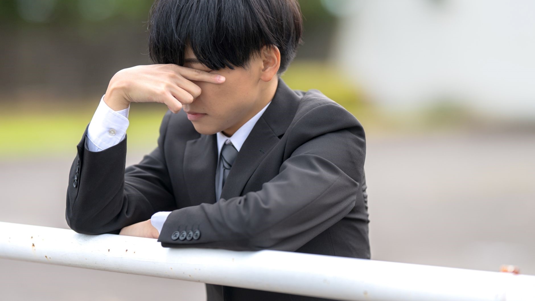 外、手すり、顔を手で覆うスーツの男性