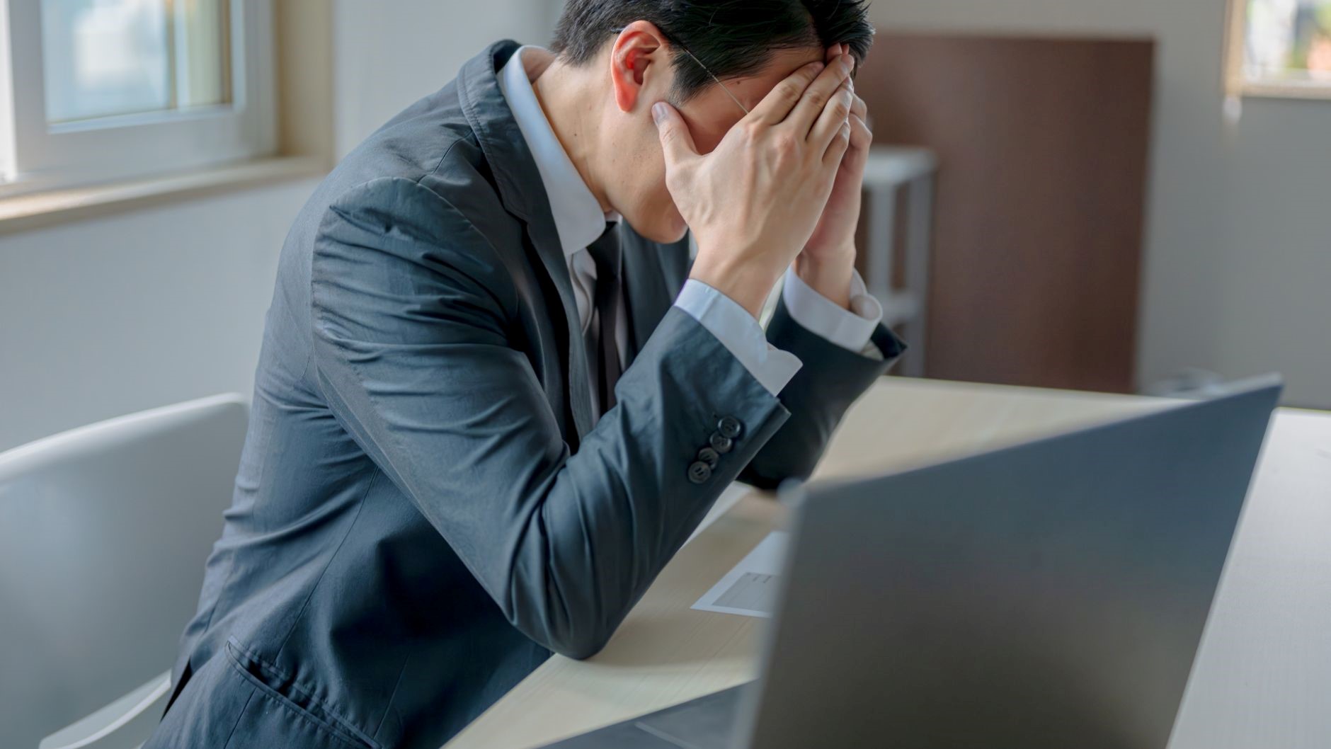 手で顔を覆う眼鏡の男性、PC