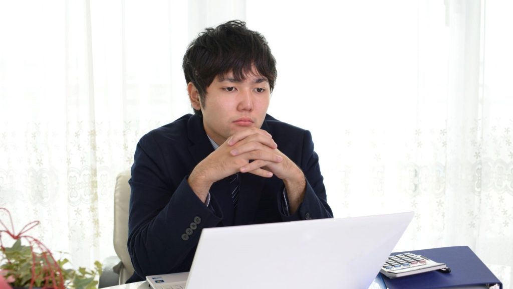 PCの前で肘をついて考える男性