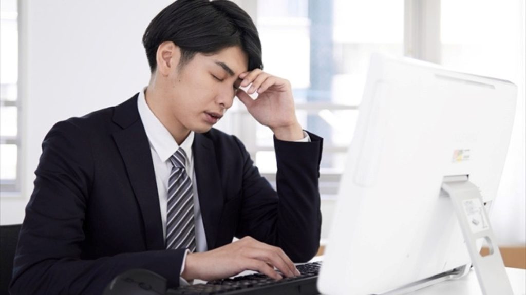 PCの前で頭を抱えて悩む男性
