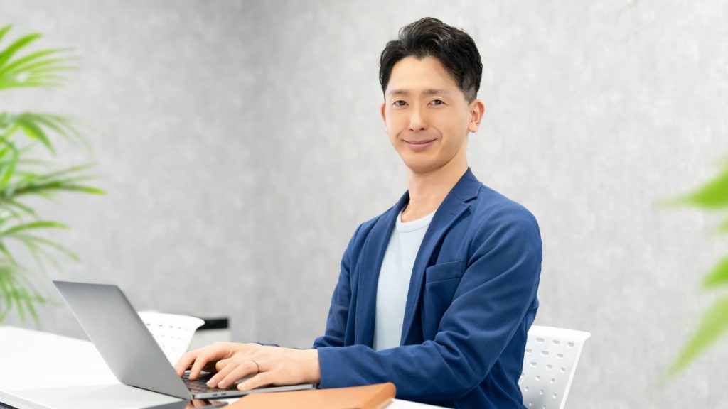 PCのキーボードに手を添えて笑顔を向ける男性