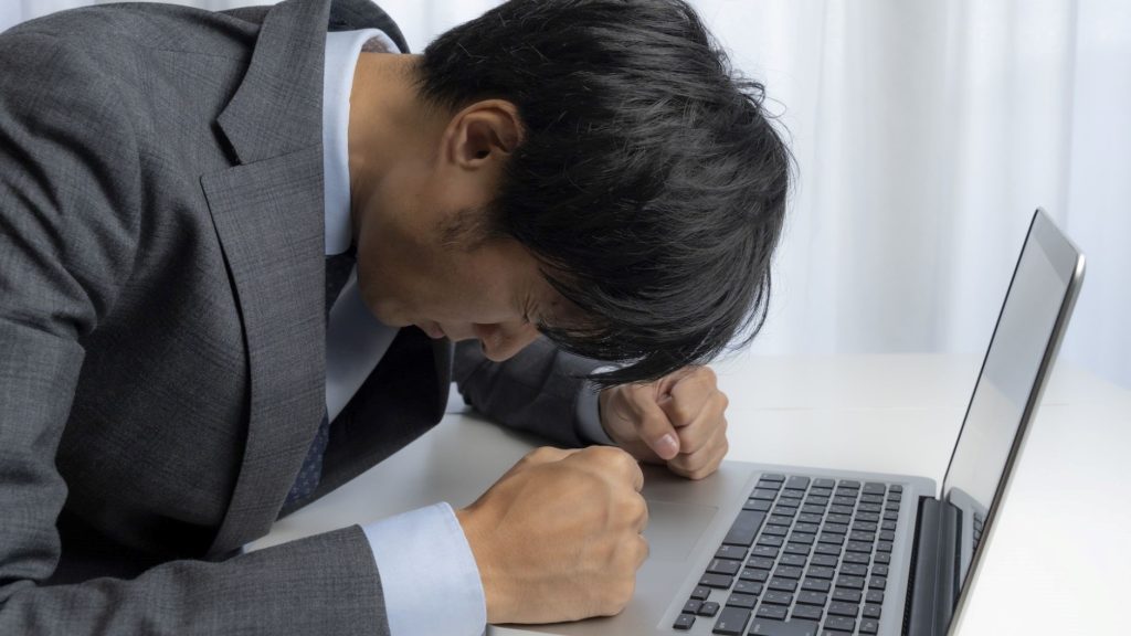 机で前かがみになって落ち込む男性