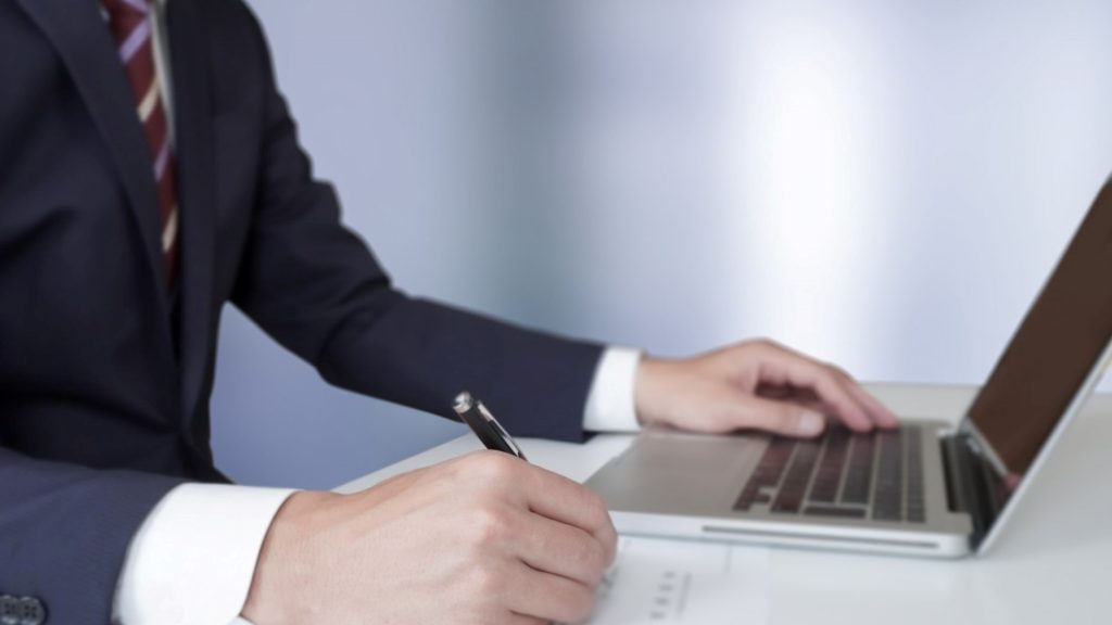 PCで文字を打つ手と手書きで書類を書く手元