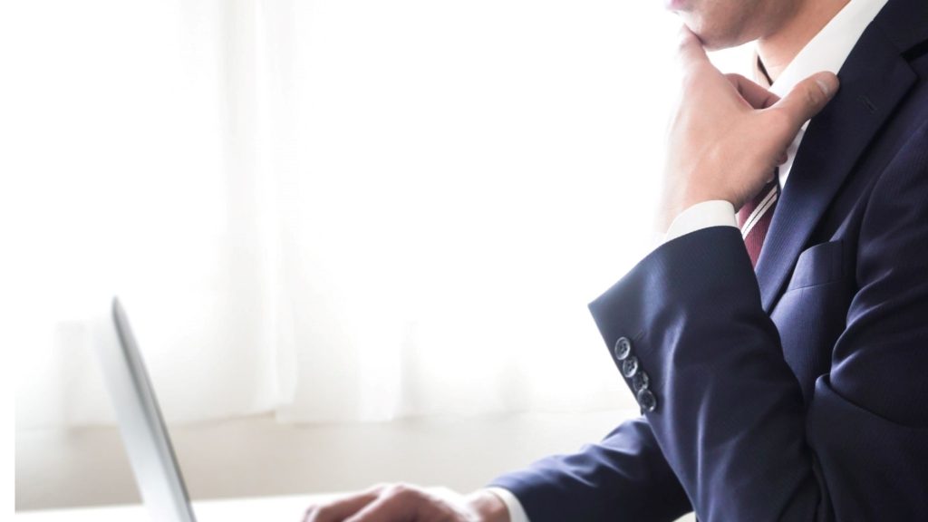 PCの前で顎に手を当てて悩む男性