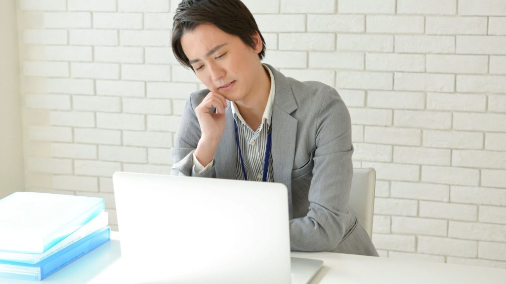 PCの前で肘をついて悩む男性
