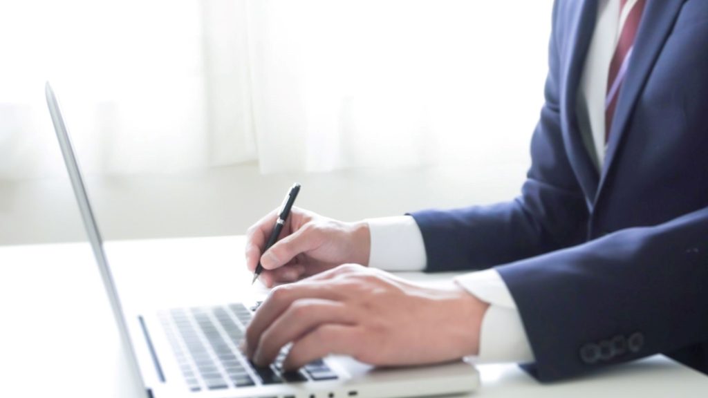 片手でPCで文字を打ち、反対の手でペンで文字を書いている手元