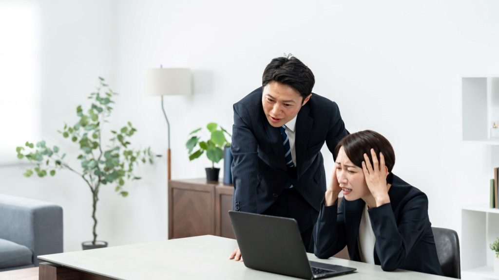 PCの前で頭を抱える女性とその画面をのぞき込む男性