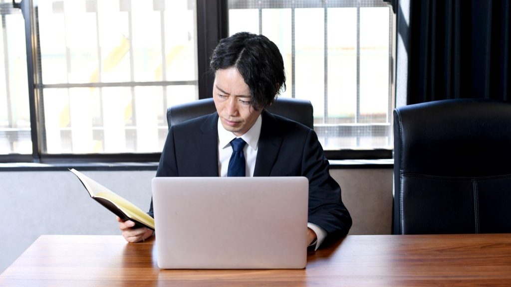 PC操作をしながらノートを開く男性