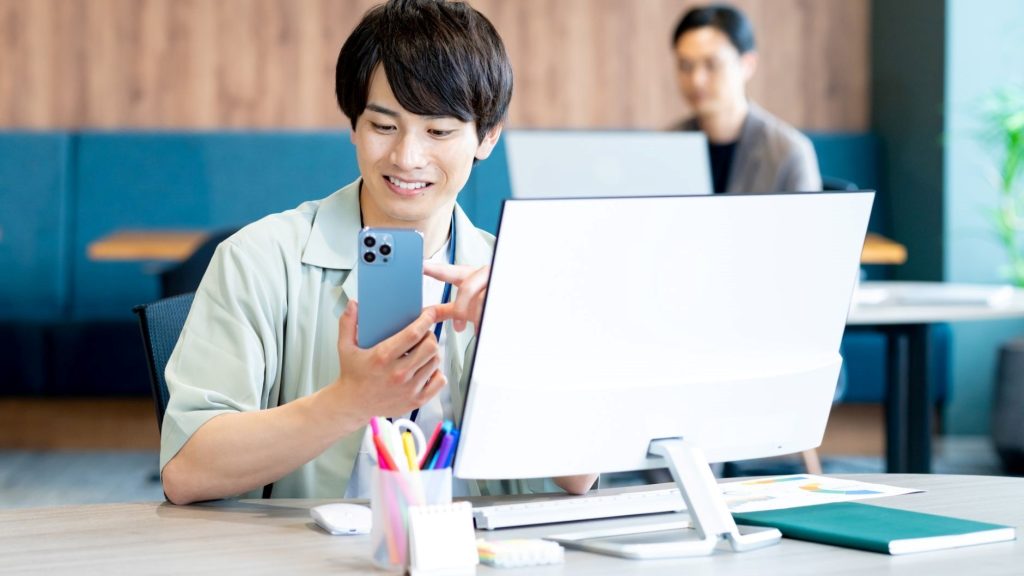 PCの前でスマホを操作する男性