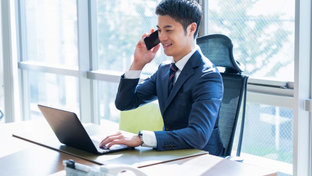 PCの前でスマホ通話をする男性