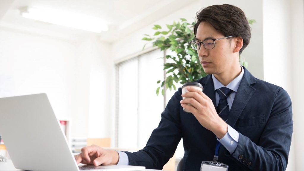 PCを操作しながらコーヒーを飲む男性