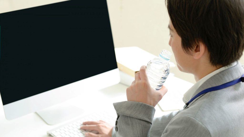 PCの前で水を飲む男性