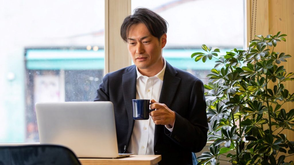 コーヒー片手にPCを操作する男性