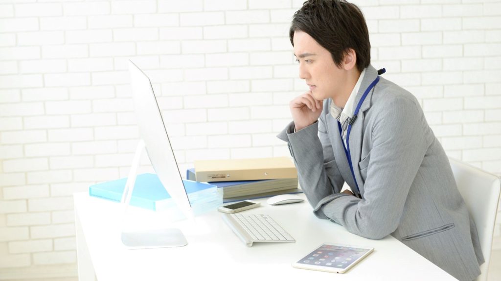 PC画面を見て悩む男性