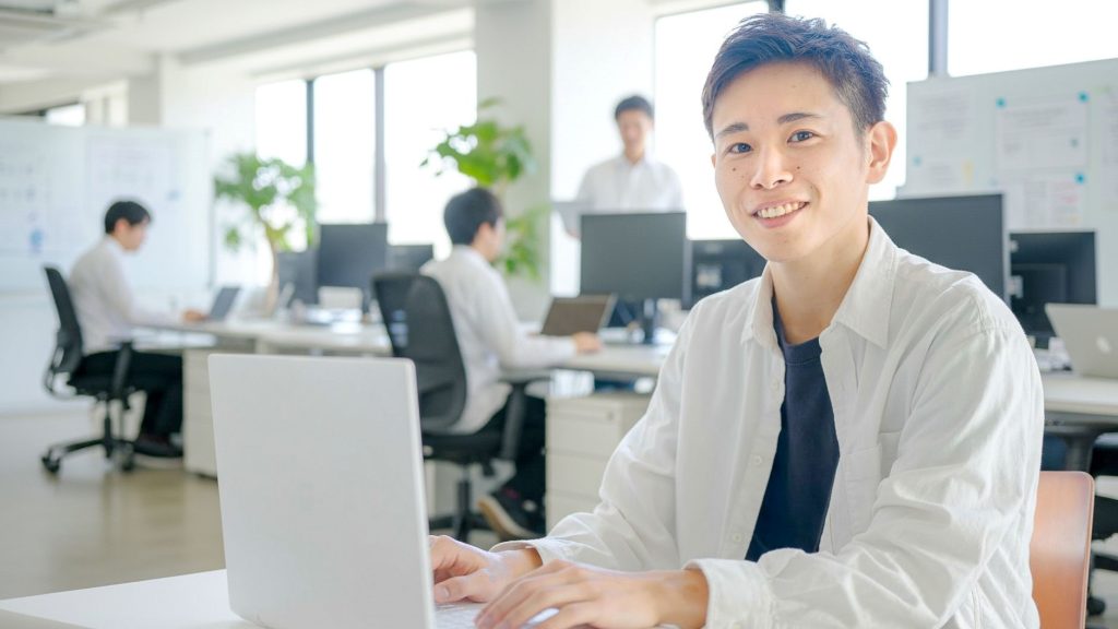 PCに手を添えて笑顔を向ける男性